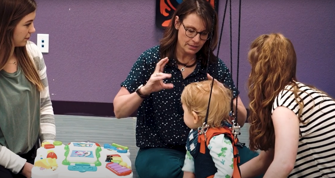 physical therapy professor instructs students while working with toddler patient