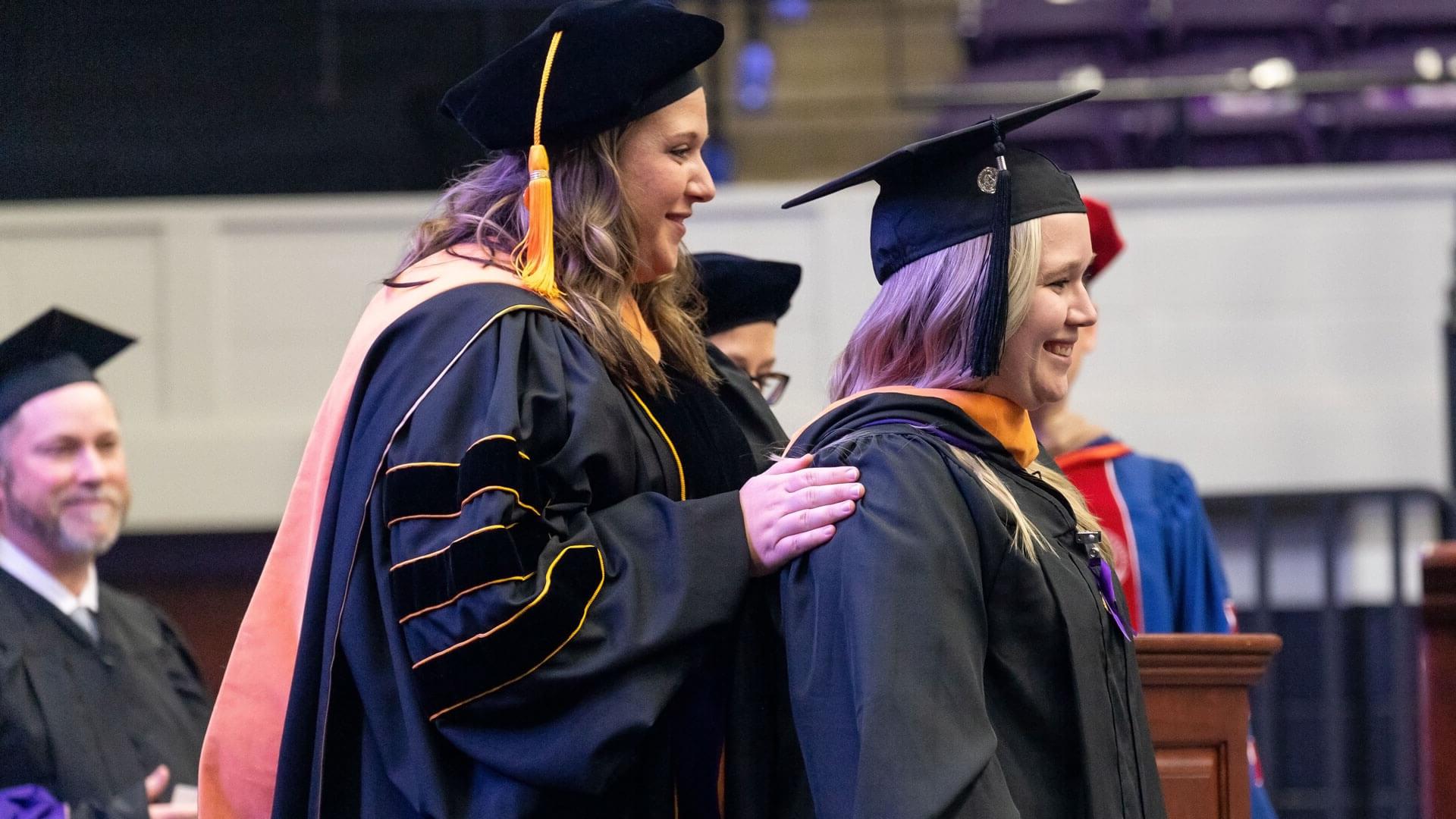 nursing graduate receives master's hood from professor during commencement ceremony