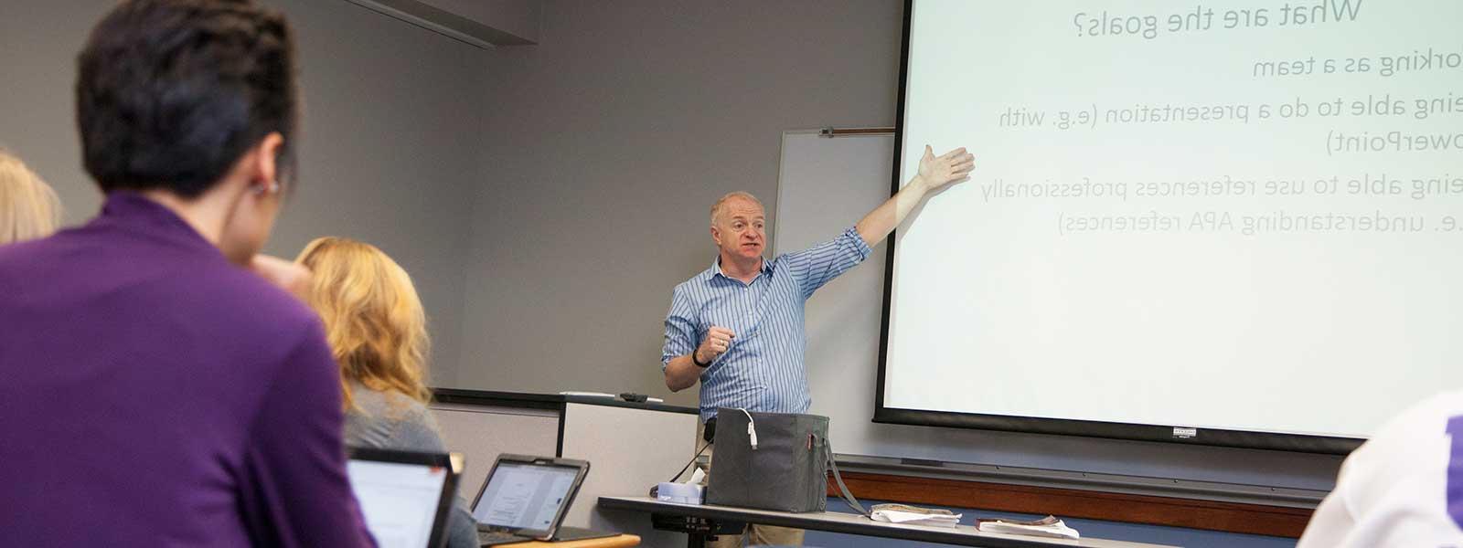 sociology professor gives class lecture while students take notes on laptops